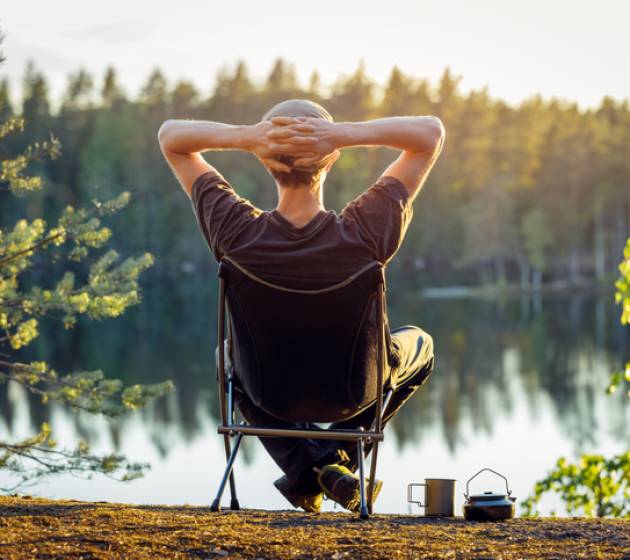 Man is sitting in a camping chair on the background of a forest lake on a beautiful summer evening.  Object in focus, background blurred.